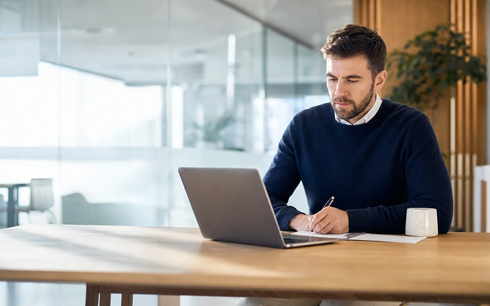 Mężczyzna pracuje przy laptopie i robi notatki podczas szkolenia online.