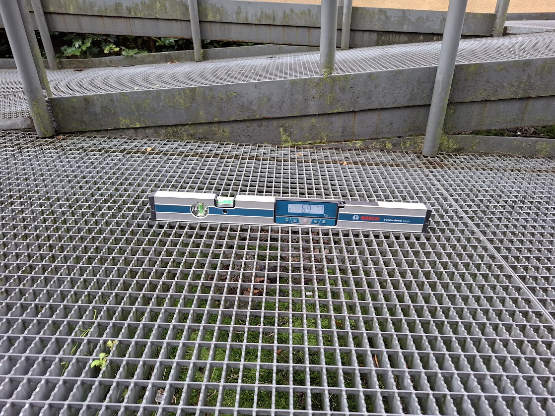 Poziomica elektroniczna na metalowej kracie podczas sprawdzania równości dojścia.