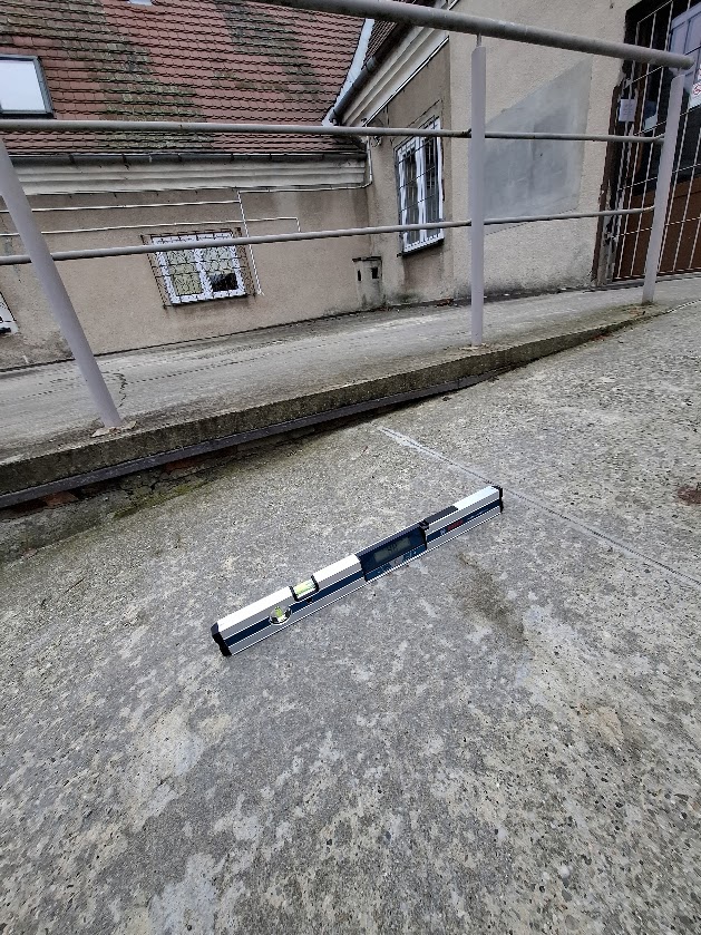 Poziomica elektroniczna mierzy nachylenie betonowej pochylni prowadzącej do wejścia.